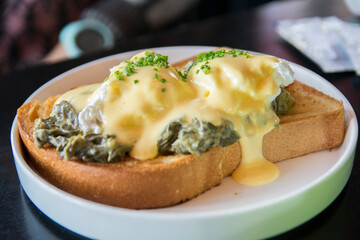 Traditional Eggs Benedict Florentine with poached eggs. creamed spinach, green onions, Hollandaise sauce and nutmeg, over a brioch bread`