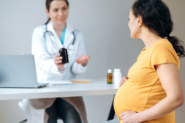 Fototapeta premium Healthcare of pregnant adult woman. Mixed race pregnant woman in sits at doctor's appointment, receiving consultation and treatment, defocused female doctor sitting at a table giving consultation