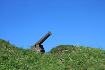 Old black cannon in wooden base on green grass hill on the background of cloudless blue sky