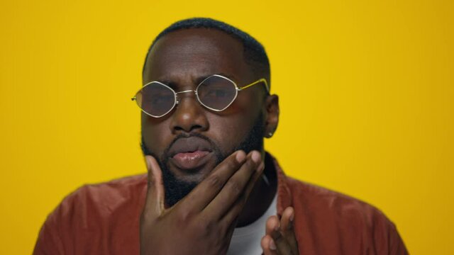Portrait of serious african american man checking beard on yellow background. 