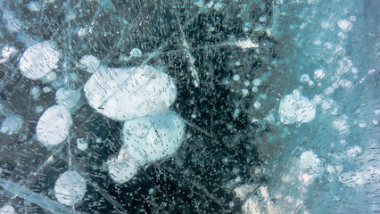 Transparent turquoise ice of Lake Baikal. Top view. Cracks and numerous frozen bubbles are visible - large and small. Full screen.