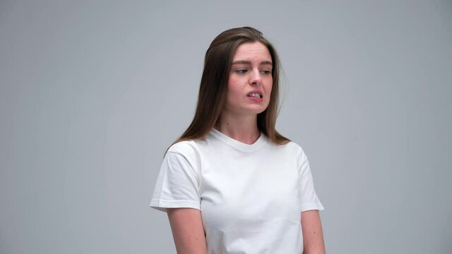 Portrait of funny confused thoughtful shy shamed young girl 20s woman wearing white t-shirt bite lips saying oups I am sorry isolated on white grey background in studio. Natural beauty and emotions.