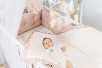 Fototapeta na wymiar Portrait of a cute 6-month-old baby, a newborn girl lying in a baby crib