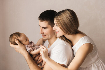 Woman and man holding a newborn. Mom, dad and baby. Close-up. Portrait of young smiling family with newborn on the hands. Happy family on a background.
