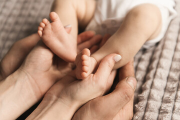 Portrait of a cute bab, the legs of a newborn in the hands of dad and mom