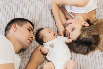 Woman and man holding a newborn. Mom, dad and baby. Close-up. Portrait of young smiling family with newborn on the hands. Happy family on a background.