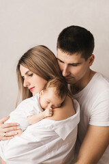 Fototapeta premium Woman and man holding a newborn. Mom, dad and baby. Close-up. Portrait of young smiling family with newborn on the hands. Happy family on a background.
