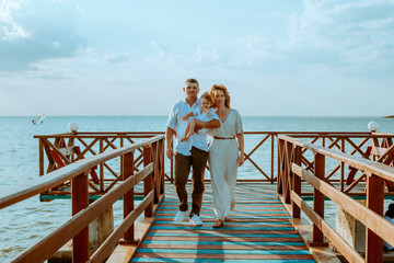 A young family with a little daughter, a toddler, in light clothes in the summer on the seashore, enjoy their vacation. Happy family and children. Summer vacation and tourism