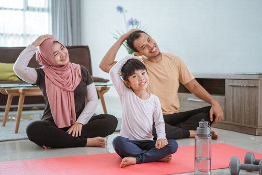 Beautiful Asian Muslim Family Exercising At Home Together. Parent And Child Doing Sport Stretching In Livingroom