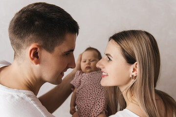 Woman and man holding a newborn. Mom, dad and baby. Close-up. Portrait of young smiling family with newborn on the hands. Happy family on a background.