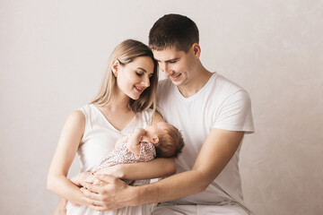 Woman and man holding a newborn. Mom, dad and baby. Close-up. Portrait of young smiling family with newborn on the hands. Happy family on a background.