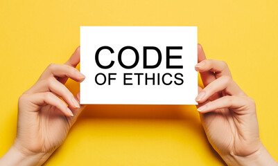 Female hands hold card paper with text Code of Ethics on a yellow background. Business and finance concept