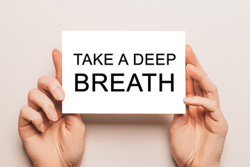 Female hands hold card paper with text Take a deep breath on a yellow background. Business and finance concept