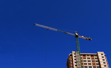 Multi-storey new house and construction crane on a background of blue sky, bottom view