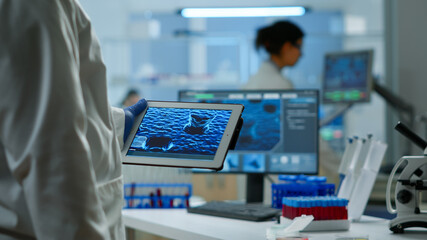 Close up of scientist in lab coat working holding tablet standing in modern equipped laboratory. Team chemists examining vaccine evolution using high tech and chemistry tools for virus development