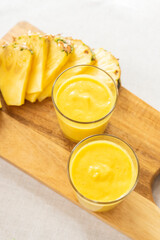Mango with pineapple smoothie in jug and glasses. Fresh morning breakfast on the table for slimming with yellow fruit