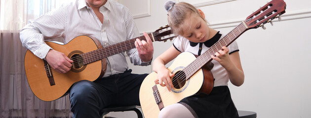 little girl and her father are playing guitar. Learning to play the guitar. Music education and extra-curricular lessons.