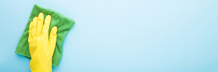 Hand in rubber protective glove with dry rag wiping table, wall or floor surface in kitchen,...