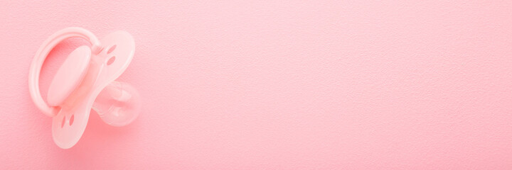 One silicone baby soother on light pink table background. Pastel color. Closeup. Wide banner. First newborn toy. Empty place for text. Top down view.