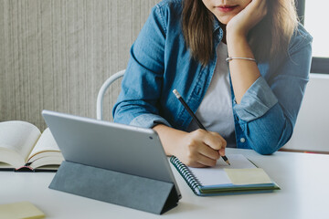 Young asian woman, girl student high school study take notes, learn online academic lesson in university library, home or house on touchpad, tablet. Concept technology of education.