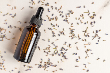 Dropper bottle of lavandula essential oil, scattered flowers of dried purple lavender blossom on...