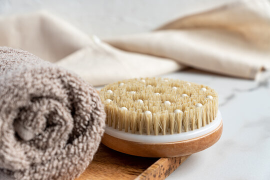 Close up of a bath bamboo brush for dry massage and cotton towel on a wooden tray on marble background. Home spa and relaxation tools.