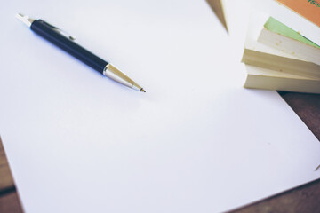 Blank sheet of paper and pen on wooden desk and blurred background.