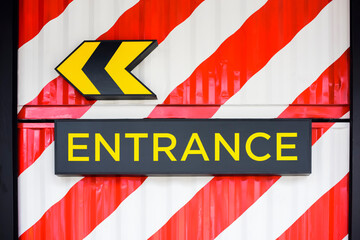 ENTRANCE word with arrow sign on red and white container wall background.