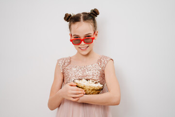 teen girl with glasses to watch 3D movies eats popcorn against white wall.