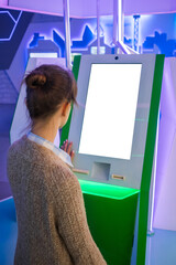 Woman looking at vertical digital interactive white display kiosk at exhibition or museum with...