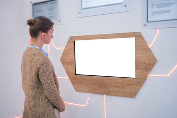 Woman looking at blank digital interactive white display wall at exhibition, museum with futuristic...