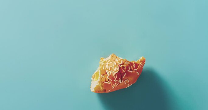 Perfect orange glazed doughnut fast eats over blue background. Eating delicious sweet donut with white sprinkles on blue. Timelapse. Top view or flat lay doughnut stop motion. Food concept 4K UHD