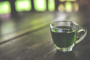 a glass of hot green tea on wooden table with blur bright green nature