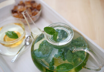 Fresh brewed mint tea on tray with teacup teapot and candi sugar healthy living