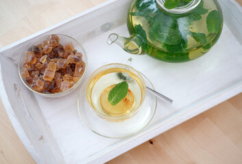 Fresh brewed mint tea on tray with teacup teapot and candi sugar healthy living