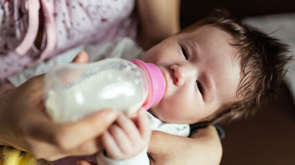 A mother feeds her newborn baby with infant formula from a bottle, the girl is one month old. Artificial feeding concept.