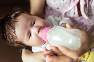 A mother feeds her newborn baby with infant formula from a bottle, the girl is one month old. Artificial feeding concept.