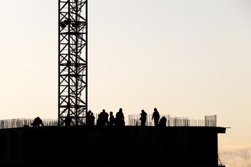 Obraz premium Silhouettes of workers on construction site against the sky. Housing construction, builders working on scaffolding