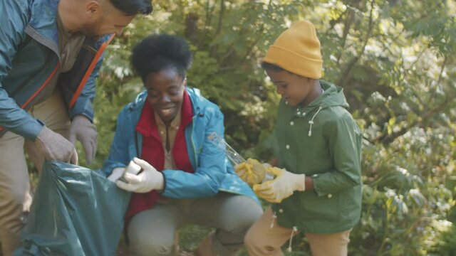 Little mixed race boy in protective gloves helping multiethnic mother and father with cleaning up campground before leaving