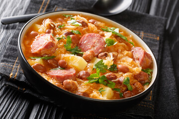 Portion of Jota sauerkraut with borlotti beans, potatoes and sausages close-up in a bowl on the table. horizontal