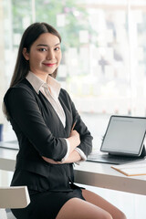 Portrait of young asian businesswoman sitting with crossed arms, smiling and looking at camera.