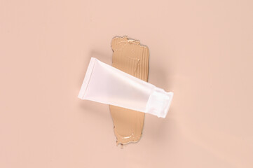 Concealer mat tube and cream smear on pink background. Beige foundation swatch.