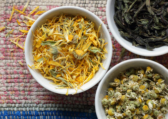 Calendula, chamomile and willowherb - dry herbs in bowls on bright woven rustic textured fabric of pink with blue color, closeup, from above overhead top view flat lay, naturopathy homeopathy  concept