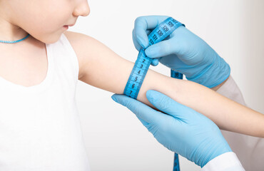 Doctor nutritionist measures the thickness of the child's hand with a measuring tape. The concept of being too thin, underweight, close-up.