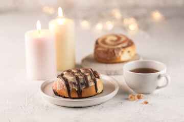 Sinabon buns with chocolate on a flat plate with a cup of tea, candles and a garland bokeh on a light background.
