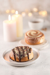 Sinabon buns with chocolate on a flat plate with a cup of tea, candles and a garland bokeh on a light background.