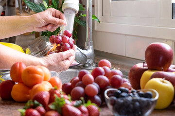 Group of fresh red fruit and woman's hands washing grape under the jet of water