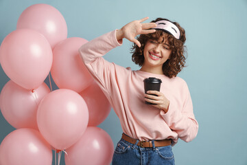 Happy woman gesturing and drinking coffee while posing with pink balloons © Drobot Dean