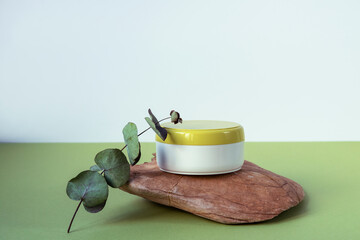 White jar of cream with a green lid and a branch of eucalyptus on a natural stone. Copy space