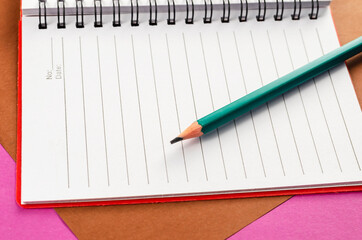 Open spring-loaded notebook and pencil on a pink and brown backg